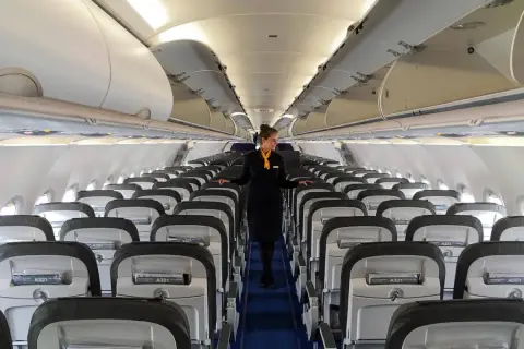 Flugbegleiterin in einem leeren Flugzeug. Die Reihen von Sitzen und die sorgfältige Präsentation lassen die Frage "Ist Lufthansa sicher?" positiv beantworten.