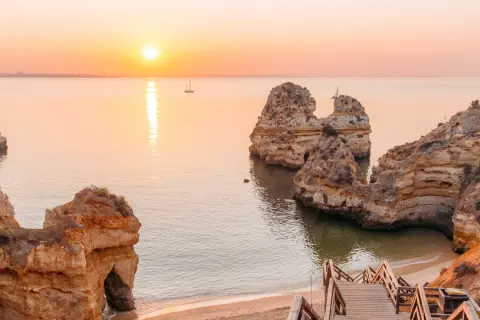 Sonnenuntergang an der Algarve: Ein perfekter Urlaub in Portugal am Meer mit Felsformationen und einer Holztreppe zum Strand.