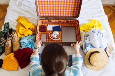 Packliste Mallorca: Koffer wird mit Kleidung, Schuhen, Kopfhörern, Reisepass und Laptop gepackt.
