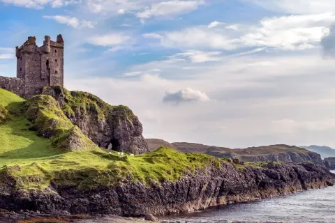 Ruinen einer Burg auf einem grünen Hügel über dem Meer. Schafe grasen friedlich. Was sollte man in Schottland nicht tun? Nicht hierher reisen!