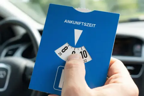 Blaue Parkscheibe mit Ankunftszeit-Einstellung im Auto. Beachten Sie die Regeln zum Parken mit Parkscheibe nach 18 Uhr.
