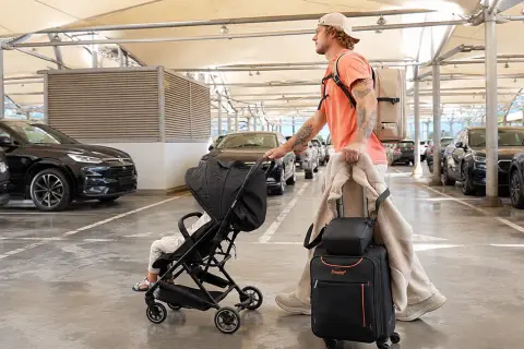 Mann mit Gepäck und Kinderwagen auf dem Parkplatz eines Flughafens.