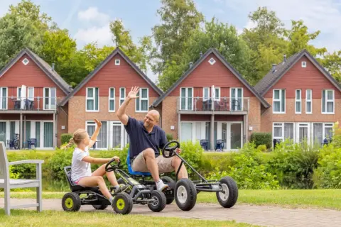 Vater und Tochter winken fröhlich, während sie mit Go-Karts durch die Anlage des TUI Kids Club fahren.