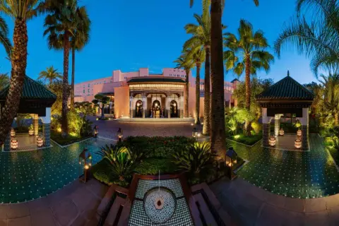 Eingangsbereich des La Mamounia Hotels in Marrakesch bei Dämmerung, umgeben von Palmen und beleuchteten Pavillons.