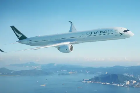 Cathay Pacific Sicherheit: Ein modernes Flugzeug fliegt über einer Stadt und dem Meer.