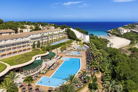 Blick auf das TUI Kids Club Cala Mandia Resort mit Pools, Strand und Meer.