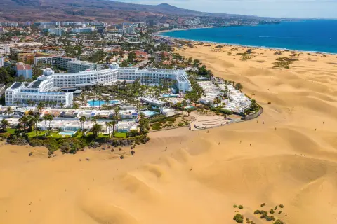 Das Riu Palace Maspalomas thront majestätisch am Rande der goldenen Dünen, mit dem blauen Meer im Hintergrund.