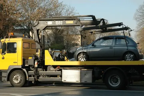 Gelber Abschleppwagen mit grauem Kleinwagen auf der Ladefläche. Ein unerwarteter Stopp, die abschleppkosten 400 euro sind ärgerlich.