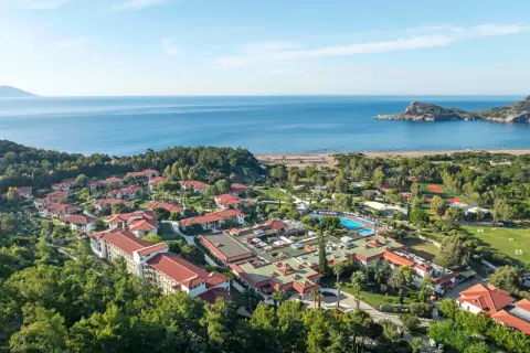 Luftaufnahme des TUI Blue Sarigerme Park mit Blick auf das Meer, Pools und Tennisplätze, eingebettet in üppige grüne Bäume.