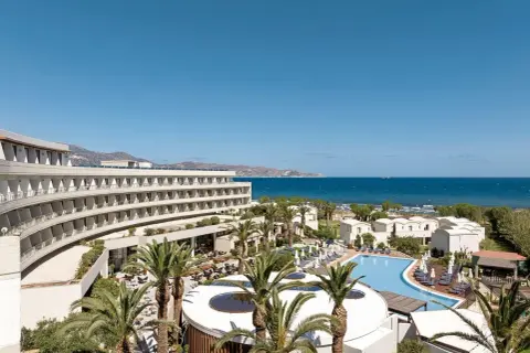 Agapi Beach Resort mit geschwungener Architektur, Pool und Palmen am Meer.
