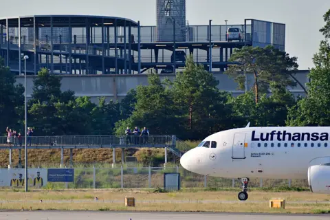 Lufthansa Airbus A320-200 auf dem Rollfeld in Frankfurt. Im Hintergrund ein Parkhaus und Bäume.
