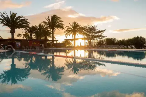 Sonnenuntergang am Robinson Esquinzo Playa. Palmen spiegeln sich im Pool.