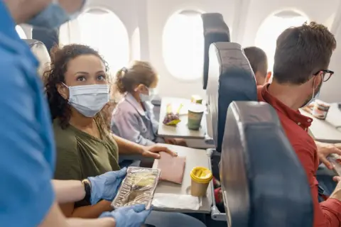 Fliegen mit FFP2-Maske: Eine Frau erhält ihr Essen im Flugzeug. Andere Passagiere tragen ebenfalls Masken.