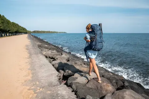 Frau mit großem Rucksack wandert über Felsen am Meer. Perfekte Packliste für Bali!