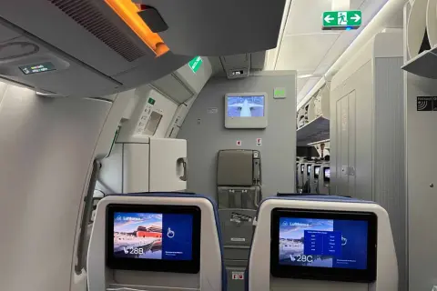 Blick in die Flugzeugkabine. Bildschirme zeigen "Lufthansa" und Sitzplatz 28B/C. Hier erfährst du, wo man im Flugzeug am besten sitzt.