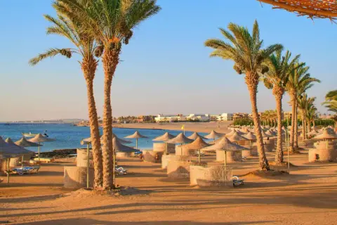 Sonnige Strandkulisse in Hurghada mit Palmen, Sonnenschirmen und Liegen. Perfekt für die Packliste Hurghada!