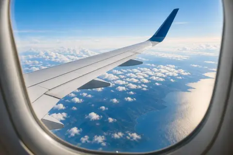 Flugzeugfenster mit Blick auf Flügel, Wolken und Küste. Ein Gabelflug ist eine Reise mit zwei Zielen.