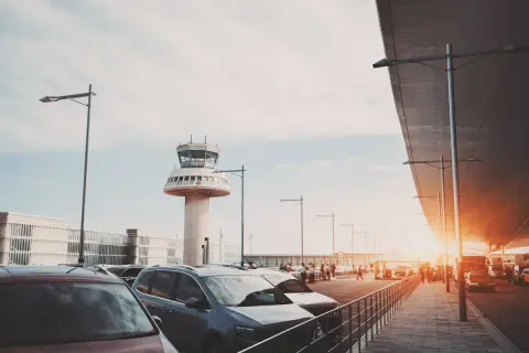 Autos parken am Flughafen Barcelona, mit dem markanten Kontrollturm im Hintergrund.