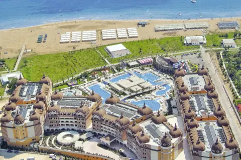 Luftaufnahme eines luxuriösen Resorts mit Kuppeldächern, Pools und Wasserrutschen, das an einen Strand grenzt. Ein Hauch von royal alhambra palace.
