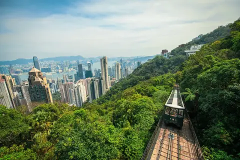 Blick auf die Skyline von Hongkong mit der Peak Tram, die durch üppigen Dschungel fährt. Perfekt für einen Hongkong Urlaub!