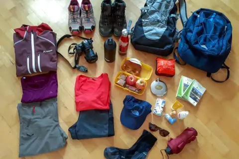 Packliste Wandern Tagestour: Kleidung, Rucksack, Kamera, Verpflegung, Trinkflasche, Wanderstiefel, Sonnenbrille, Regenschirm und Karten für die Tour.