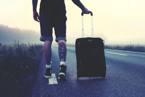 Mann mit Koffer auf einsamer Straße, bereit für London. Die Packliste ist komplett, das Abenteuer beginnt.