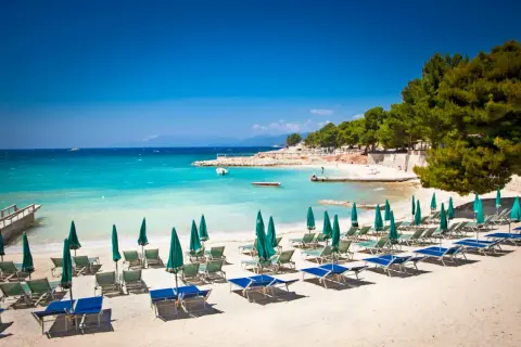 Ein sonniger **Tirana Strand** mit türkisfarbenem Wasser, Liegestühlen und Sonnenschirmen.