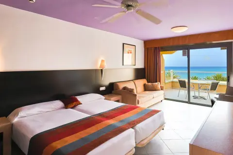 Gemütliches Zimmer im SBH Monica Beach Resort mit Meerblick. Zwei Betten, Sofa und Balkon laden zum Entspannen ein.
