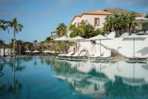 Traumhafter Poolbereich mit Liegen und Sonnenschirmen im Dreams Madeira Spa & Marina. Palmen und ein elegantes Gebäude im Hintergrund.