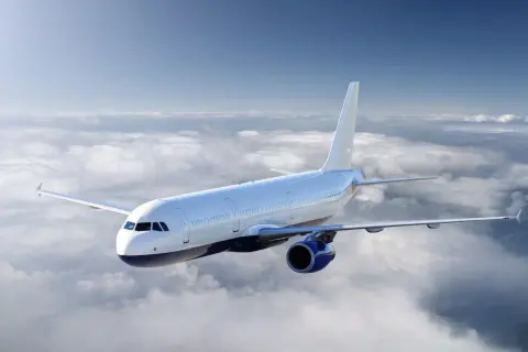 Ein weißes Flugzeug fliegt über einer Wolkendecke. Die Sonne scheint, aber die Wolken deuten auf mögliche Flugzeugturbulenzen hin.