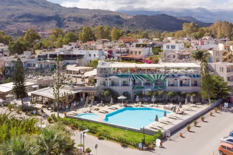 Ein **epos luxury beach hotel** mit Pool und Liegestühlen, umgeben von mediterraner Vegetation und Häusern, im Hintergrund Berge.
