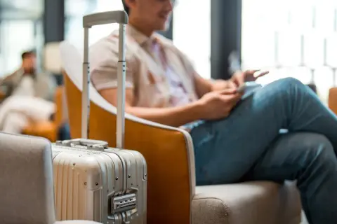Mann mit Koffer im Wartebereich, bereit für die Dienstreise. Die Packliste für die Dienstreise ist vollständig.