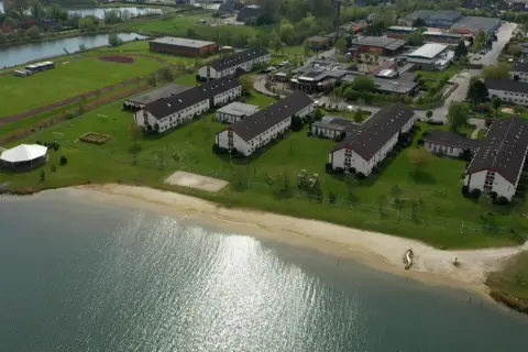 Luftaufnahme des Wangerland Resorts mit Gebäudekomplexen, einem See und einem Strand.
