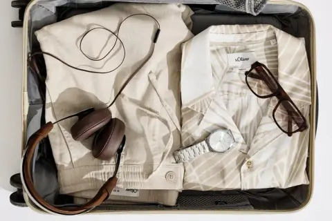 Koffer packen Liste Frauen: Leinenhose, gemustertes Hemd, Kopfhörer, Brille und Uhr für den perfekten Urlaub.