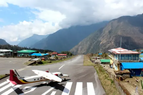 Ein kleines Flugzeug steht auf dem Rollfeld des Nepal Flughafens, umgeben von majestätischen Bergen.