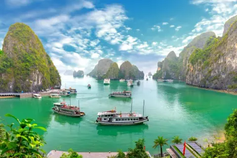 Traumhafte asien reiseziele: Boote gleiten durch smaragdgrünes Wasser, umgeben von steilen, bewachsenen Karstfelsen im Halong-Bucht.
