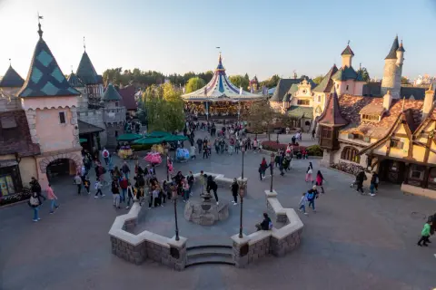Bunte Märchenhäuser und ein Karussell beleben den Platz. Eine lebhafte Menge schlendert umher, perfekt für die Disneyland-Packliste.