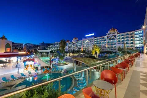 Abendansicht des Alan Xafira Deluxe Resort & Spa mit beleuchteten Pools, Palmen und stilvollen roten Stühlen auf der Terrasse.