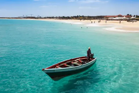 Ein Mann in einem Boot auf dem türkisfarbenen Meer vor Kapverden. Die Flugzeit dorthin lohnt sich für diesen Anblick.