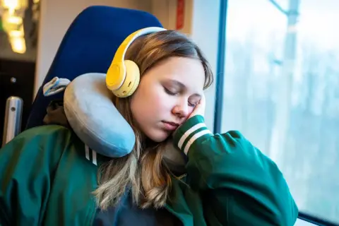 Mädchen schläft im Zug mit gelben Kopfhörern und einem Nackenkissen richtig benutzt für bequemen Halt.