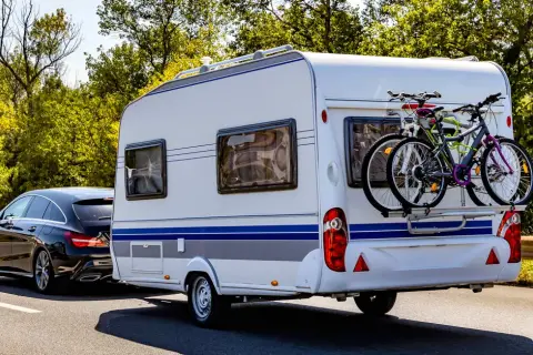 Schwarzer Kombi zieht Wohnwagen mit Fahrrädern, bereit für den Urlaub. B96 oder BE, das ist hier die Frage für die Reise.