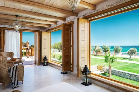 Ein luxuriöses Zimmer mit Meerblick im Mitsis Blue Domes. Eine Frau steht auf dem Balkon und genießt die Aussicht.