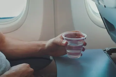 Hand hält ein Glas Wasser, während man im Flugzeug sitzt.