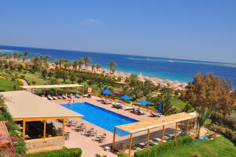 Ein luxuriöser Poolbereich mit Blick auf das Meer und den Strand des Fort Arabesque West Bay. Palmen und Sonnenschirme säumen den Weg zum türkisfarbenen Wasser.
