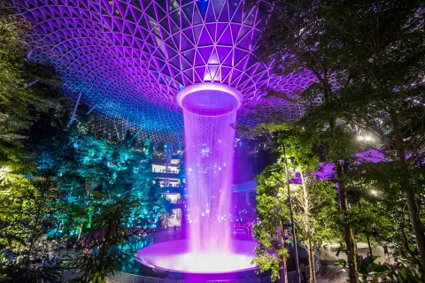 Imposanter Wasserfall im Jewel Changi Airport Singapur, beleuchtet in lila und blau unter einem geometrischen Glasdach.