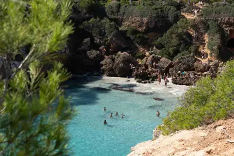 Türkisblaues Wasser in einer malerischen Bucht auf Mallorca. Menschen sonnen sich auf Felsen und schwimmen im Meer.