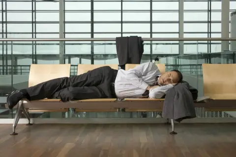 Mann schläft am flughafen auf einer Bank, sein Anzug hängt über der Lehne.