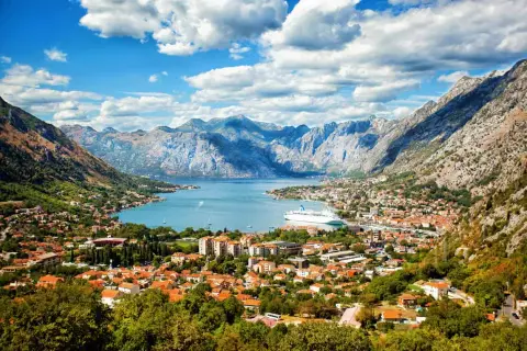 Traumhafter Urlaub in Montenegro: Die Bucht von Kotor mit Kreuzfahrtschiff und malerischer Stadt vor imposanter Bergkulisse.
