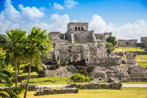 Ruinen von Tulum, ein Traumziel für jeden Mexiko Urlaub. Palmen und antike Bauten unter blauem Himmel.