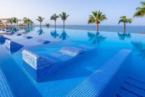 Infinity-Pool mit integrierten Liegen im Riu Gran Canaria, Palmen und Meer im Hintergrund.